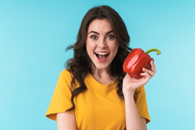 Photo emotional excited young beautiful woman posing isolated over blue wall holding paprika.