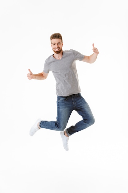 Emotional excited young man jumping showing tumbs up gesture.
