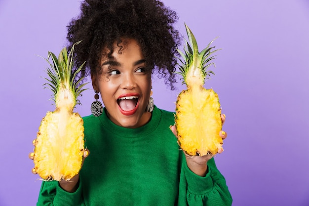 Emotional excited young pretty african woman isolated over violet space holding pineapple.