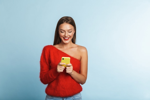 Emotional excited young woman posing isolated, using mobile phone.