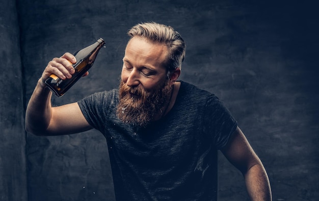 Emotional, funny redhead bearded drunk hipster male holds craft bottled beer.