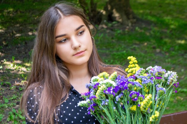 Emotional girl teenager with long hair hairstyle braids in a green shirt sits on a bench in the park