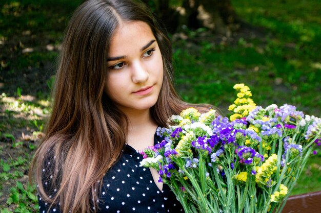 Emotional girl teenager with long hair hairstyle braids in a green shirt sits on a bench in the park