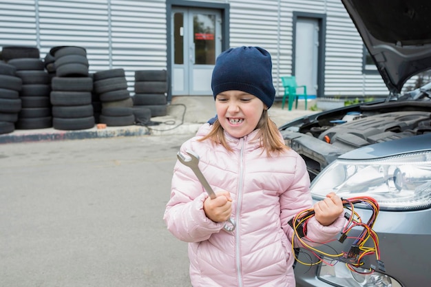 Emotional girl with a wrench and a bunch of wire at a car service Auto repair concept