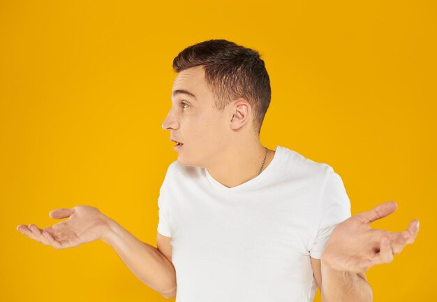 Emotional guy in a white t-shirt on a yellow background gestures with his hands portrait close-up beautiful face person