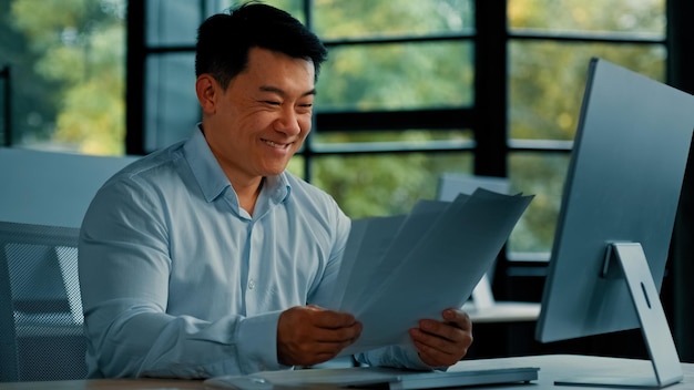 Emotional happy asian man businessman clerk specialist worker chinese korean male doing paperwork