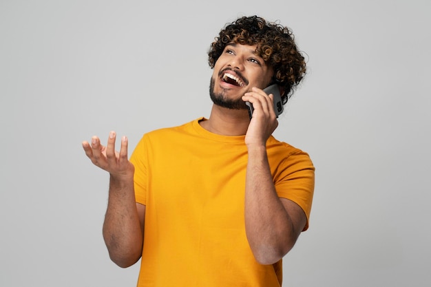 Emotional Indian man talking on mobile phone looking away, isolated on gray background. Technology