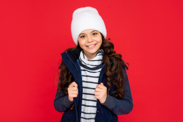 emotional kid with curly hair in hat teen girl on red background portrait of child