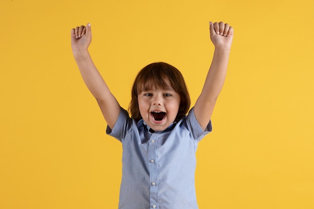 Emotional little boy shouting with raised hands enjoying win celebrating success orange studio background free space