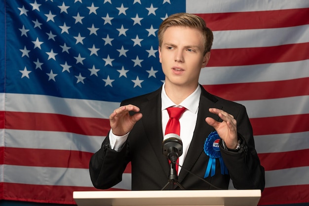 写真 アメリカの国旗を背景に演説中にトリビューンで感情的な男