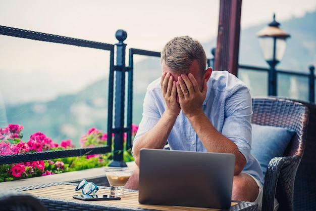 An emotional man sits at the computer on vacation and works Freelancer works while on vacation High quality photo