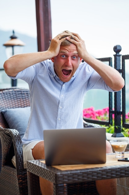 Photo an emotional man sits at the computer on vacation and works freelancer works while on vacation