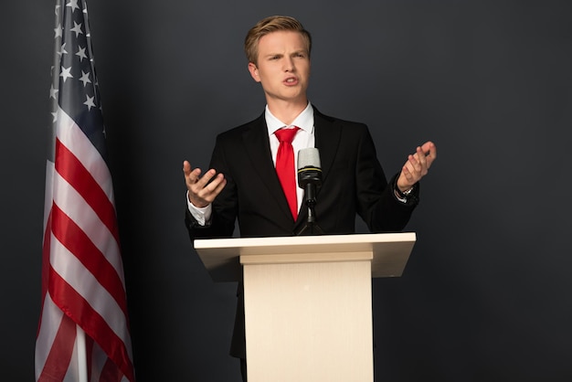 Emotional man speaking on tribune with american flag on black background