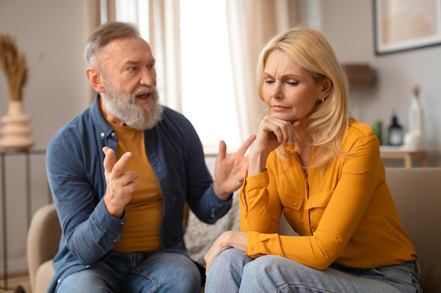 Emotional mature man gesturing shouting at his unhappy wife indoor