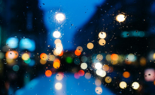 Emotional melancholic abstract background with defocused lights bokeh in London UK behind rain drops in window glass Focus on few drops due to the shallow depth of field