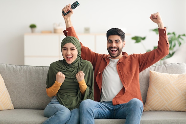Emotional middle eastern couple shouting watching sport on tv indoor
