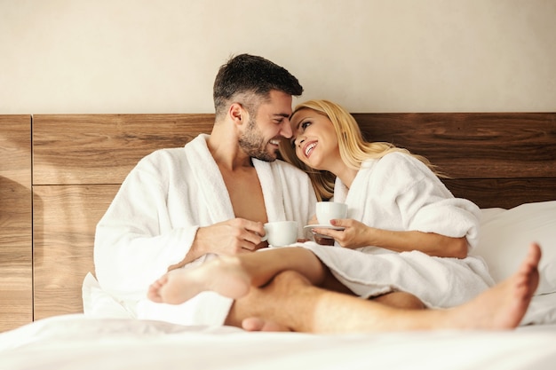 Un momento emozionante prima di un bacio. mattina di sole in una stanza d'albergo, un uomo e una donna bevono caffè e tè nel comfort di un accappatoio e di un letto caldo. amore, obiettivo della relazione, rapporto stretto