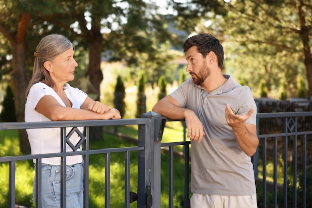 emotional neighbours having argument near fence outdoors