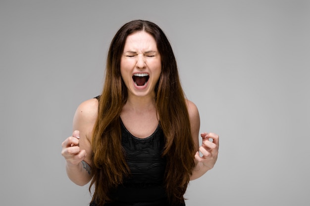 Emotional plus size model standing in studio with open mouth screaming showing agression anger want to scratch