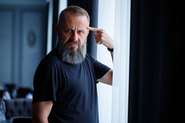 Emotional portrait of an adult gray-haired man with a beard in a black t-shirt