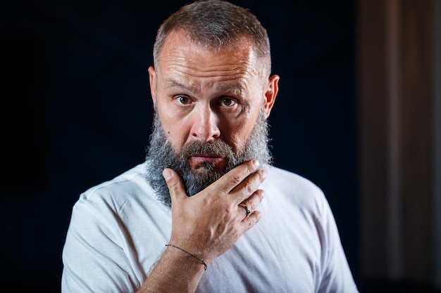 Emotional portrait of an adult gray-haired man with a beard in a white t-shirt