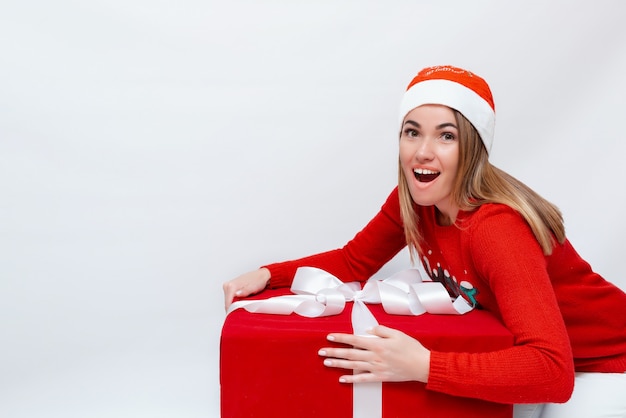 Emotional portrait of a beautiful girl in a Christmas hat and a red gift box