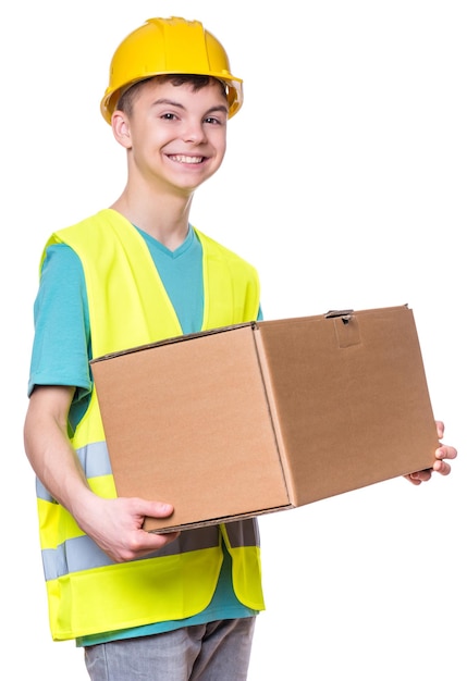안전 재과 노란색 하드 모자를 입은 잘생긴 백인 십대 소년의 감성적인 초상화 색 배경에 고립 된 큰 카드보드 상자를 들고있는 행복한 아이