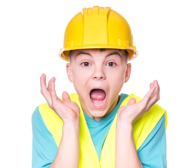 Emotional portrait of handsome caucasian teen boy wearing safety jacket and yellow hard hat Shocked child looking at camera isolated on white background Funny cute guy