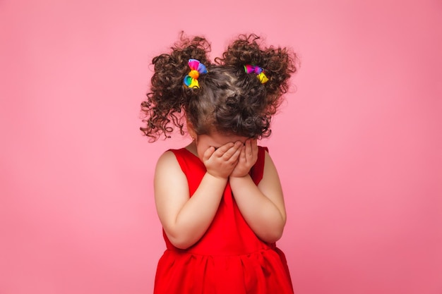 Emotional portrait of a little girl in a red dress on a pink background