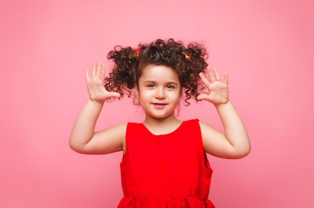 Emotional portrait of a little girl in a red dress on a pink background