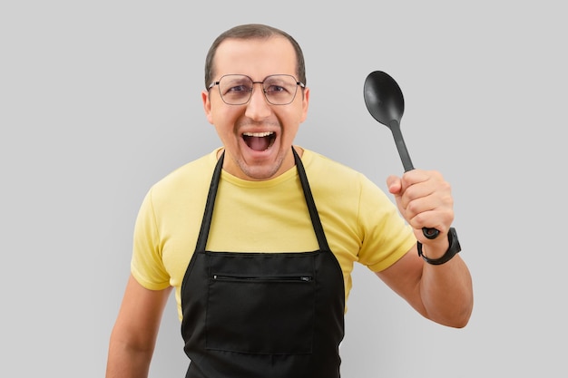 Emotional portrait of a man in an apron and a spoon in his hand on a gray background
