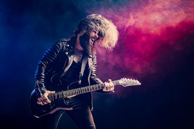 Emotional portrait of a rock guitar player with long hair and\
beard plays on the smoke background