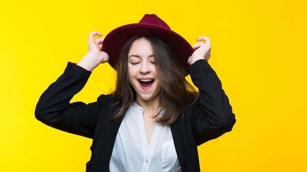 Emotional portrait of a young woman in a suit and hat on a yellow background