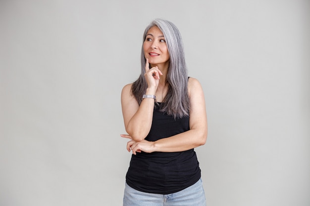 Photo emotional portraits of a paled long hair asian matured woman on grey wall