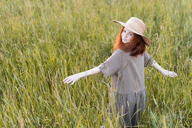Emotional redhead girl playing in the grass on a summer meadow at sunset in an elegant dress
