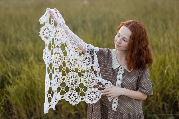 Emotional redhead girl playing in the grass on a summer meadow at sunset in an elegant dress