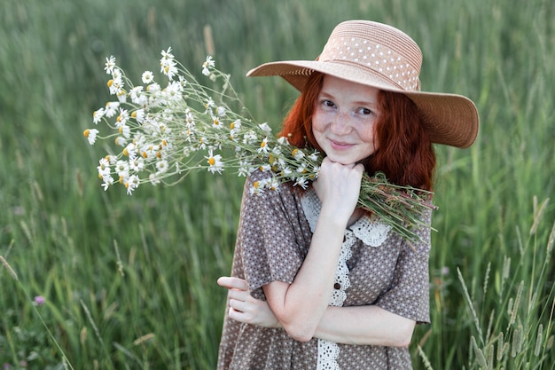 夕暮れの夏の草原の草に立っている感情的な赤毛の女の子