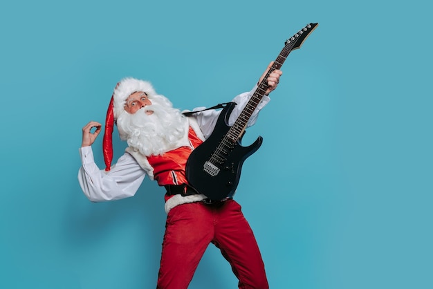 Emotional Santa musician plays on electric guitar on blue background Christmas music New Year party