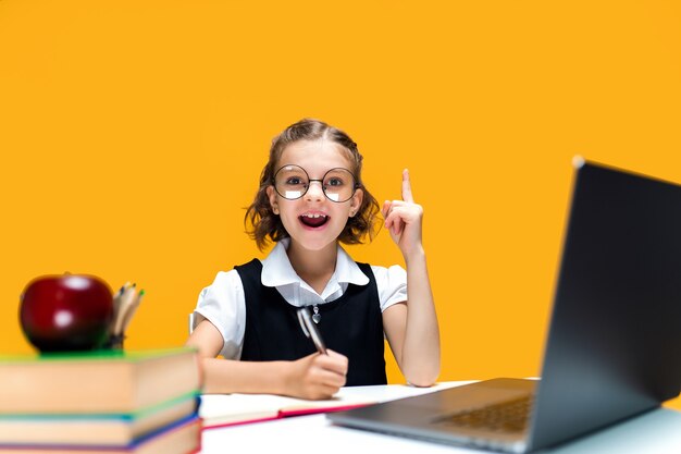 Emotional schoolgirl raises finger up sitting with laptop in glasses distance education