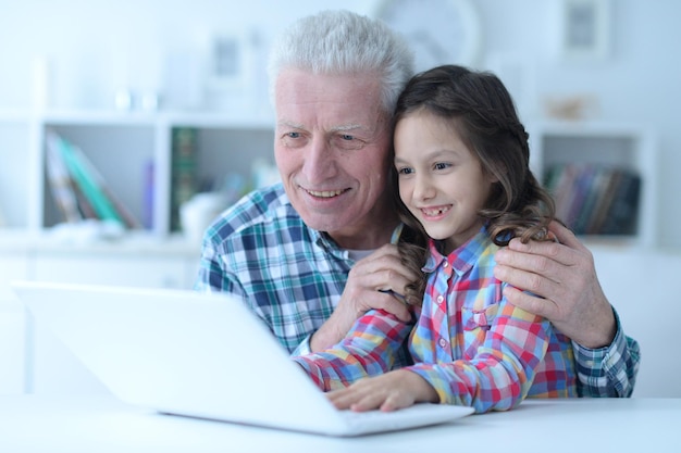 Emotional senior man with granddaughter using laptop at home