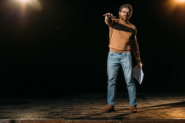 Emotional stage director holding scenario and standing on stage during rehearse in theater