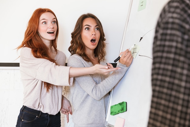 Emotional students standing in classroom indoors near desk.