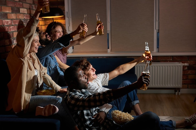 Studenti emotivi che guardano la partita sportiva a casa seduti sul divano. fan che tifano per la squadra nazionale americana preferita, bevendo birra e mangiando popcorn. concetto di emozioni, supporto.