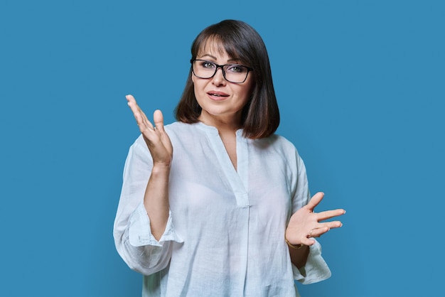 Emotional talking mature woman looking at camera on blue background