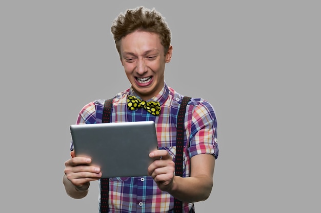 Emotional teenage boy looking at digital tablet. Expressive teen guy holding computer tablet.