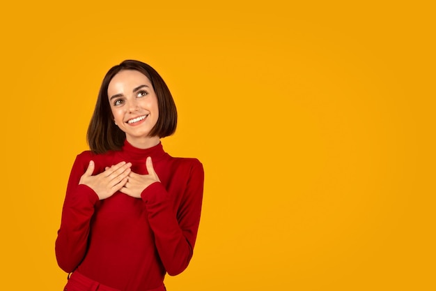 Emotional tranquil young woman holding hands on chest copy space