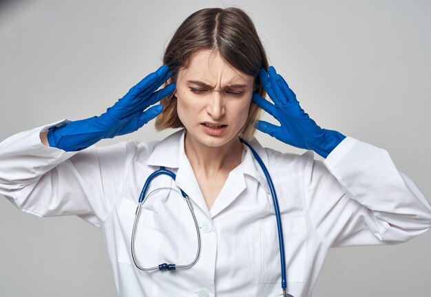 Foto la donna emotiva in guanti medici blu tocca la testa con le mani su uno sfondo chiaro