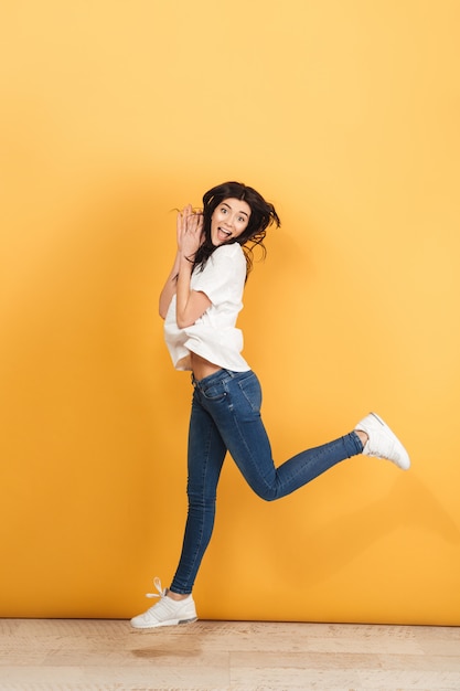Emotional woman jumping isolated over yellow wall