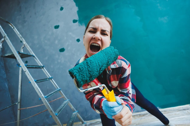 An emotional woman paints the walls Young smiling pretty woman in shirt holding roller in right hand and singing Repair in the room