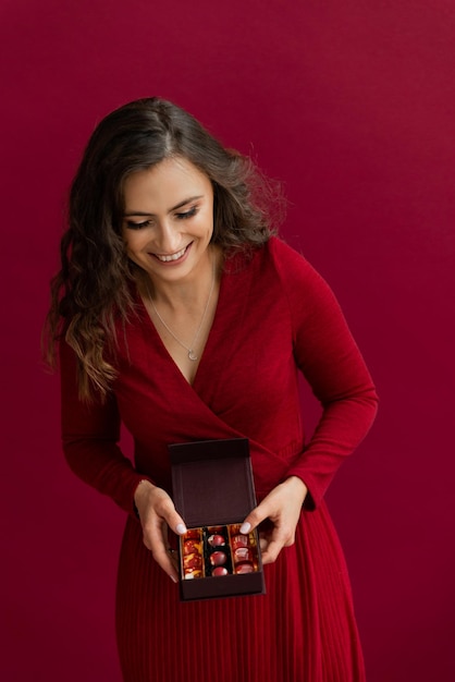 Photo emotional woman in red dress posing with little box of bonbons and happy smiling in studio